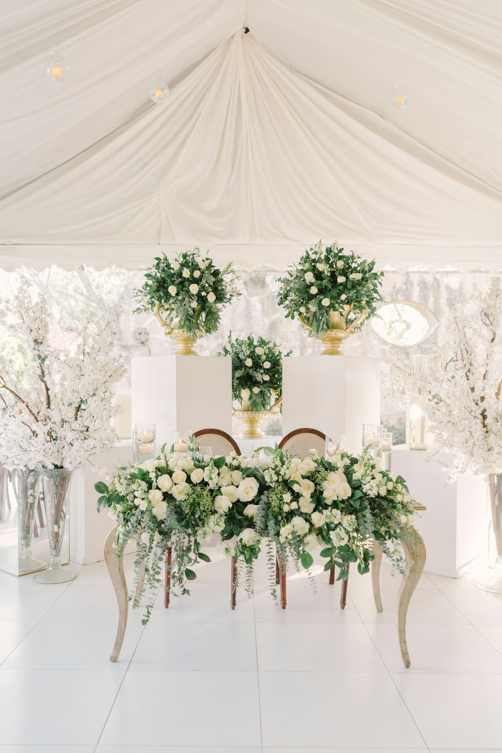 Mesa de novios bajo carpa blanca con arreglos florales verdes y blancos