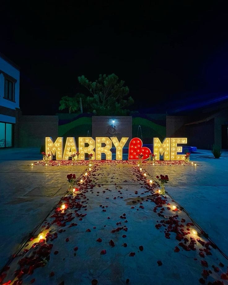 Letras luminosas Marry Me con camino de pétalos de rosa en la noche