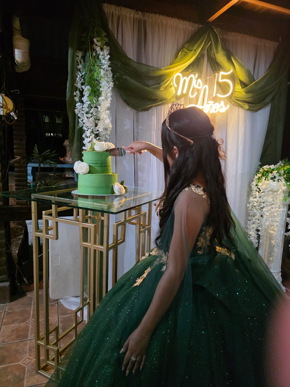 Quinceañera cortando pastel de dos pisos con letrero neón Mis 15 años