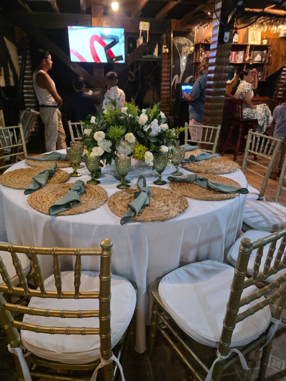 Mesa redonda con mantelería blanca, servilletas verdes y centro floral